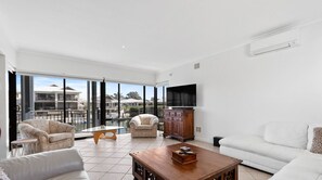 A spacious living room with a large window, a flat-screen TV, and a wooden coffee table.