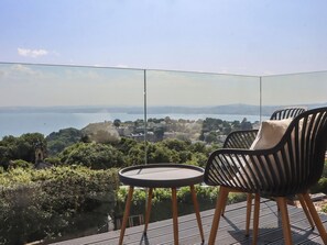 A balcony with a table and two chairs, overlooking a scenic view of a coastal town and the sea. - Seacroft (Torquay)