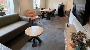 En moderne stue med en sofa, et rundt sofabord, et spiseområde med stole og et fjernsyn monteret på væggen.
