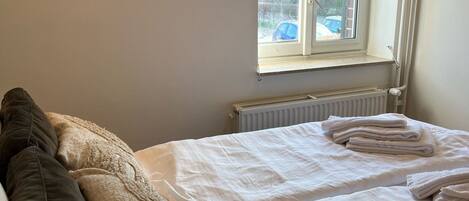 A bedroom with two beds, a radiator, a window with a view of the outside, and a ceiling fan.