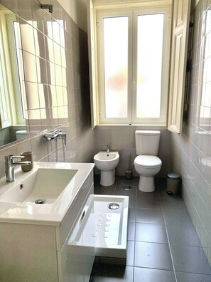 Casa de banho moderna com uma grande pia, bidé, sanita e janela com vidro jateado.