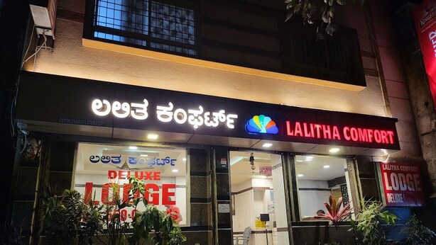 A hotel named Lalitha Comfort with a sign in a local language and English text indicating a Deluxe Lodge. - Hotel Lalitha Comfort (Bengaluru)