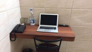 A small workspace with a laptop, a phone, a bottle of water, and a trash can. - Hotel Lalitha Comfort (Bengaluru)