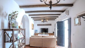 A living room with a sofa, a wooden bookshelf, a television, and a chandelier. - Apartment in Andalusia with Scenic Views (Peñaflor)