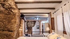 A bedroom with exposed brick walls, a wooden ceiling, a bed with a floral duvet, a bedside table, and a chair. - Apartment in Andalusia with Scenic Views (Peñaflor)