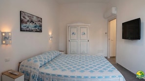 Un dormitorio con cama, un cuadro, un televisor de pared y una puerta con paneles decorativos.