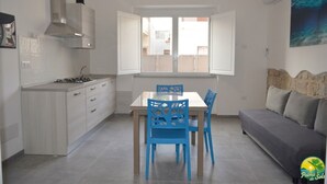 Une cuisine moderne avec des meubles blancs, une cuisinière à gaz et une fenêtre dont les volets sont ouverts.