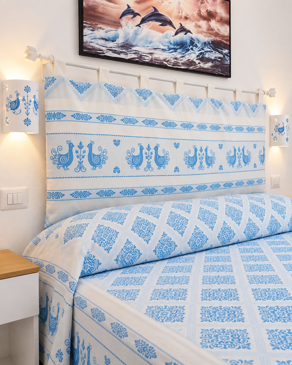 A bed with a patterned headboard and matching bedding, a bedside table, and a wall-mounted picture.