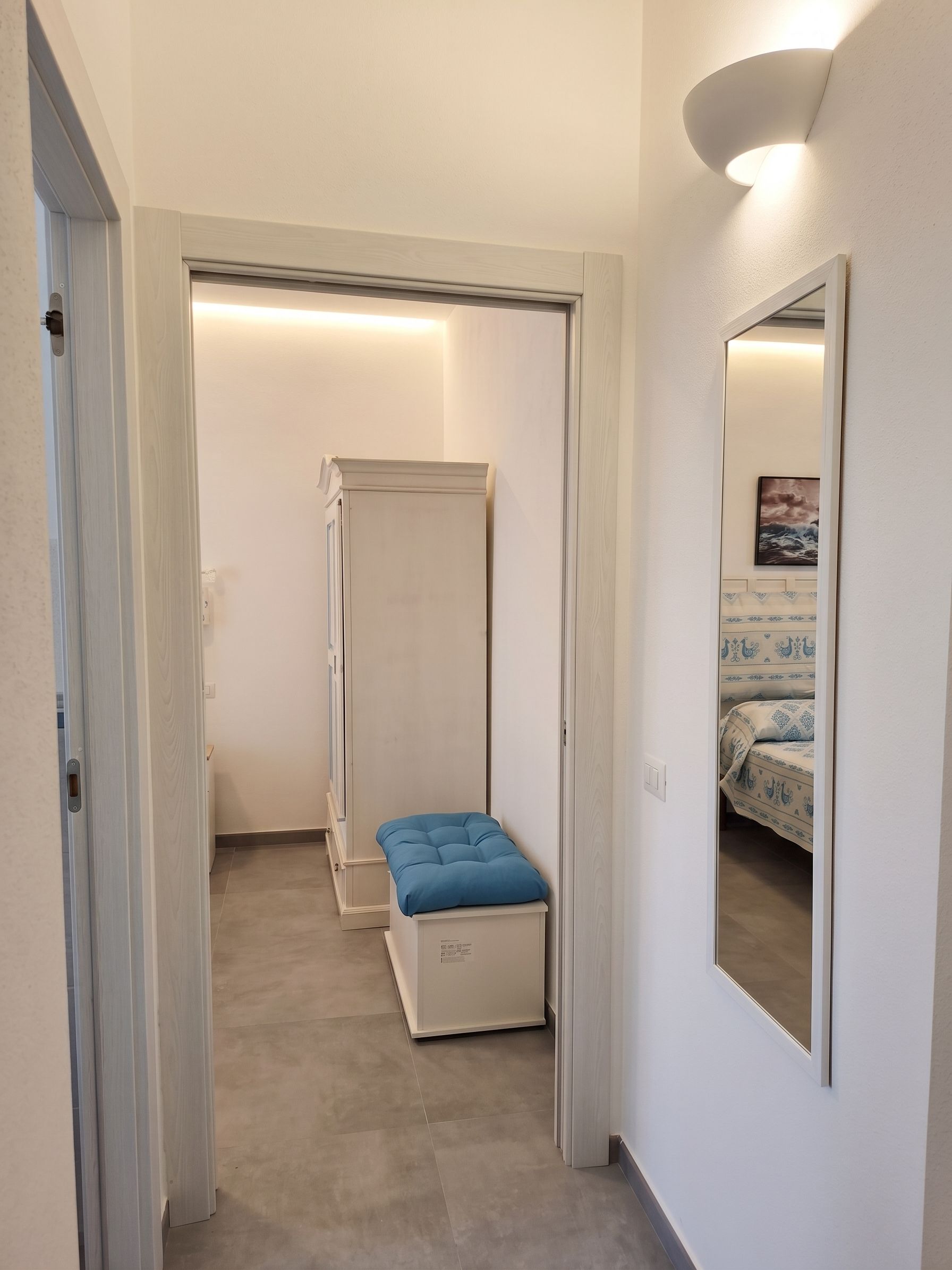 A narrow hallway leading to a bedroom with a bed and a bedside table.