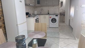 Eine kompakte Küche mit Kühlschrank, Herd, Spüle und Waschmaschine. Zwei Hocker und ein kleiner Tisch ergänzen das Bild.