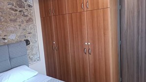 Ein Schlafzimmer mit Stehwänden, einem Bett mit grauem Kopfteil und einem Holzkasten mit mehreren Türen.