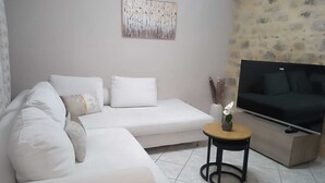 Ein modernes Wohnzimmer mit einem weißen Sofa, einem kleinen runden Tisch mit Pflanze und einem Flachbildfernseher auf einem Schrank.