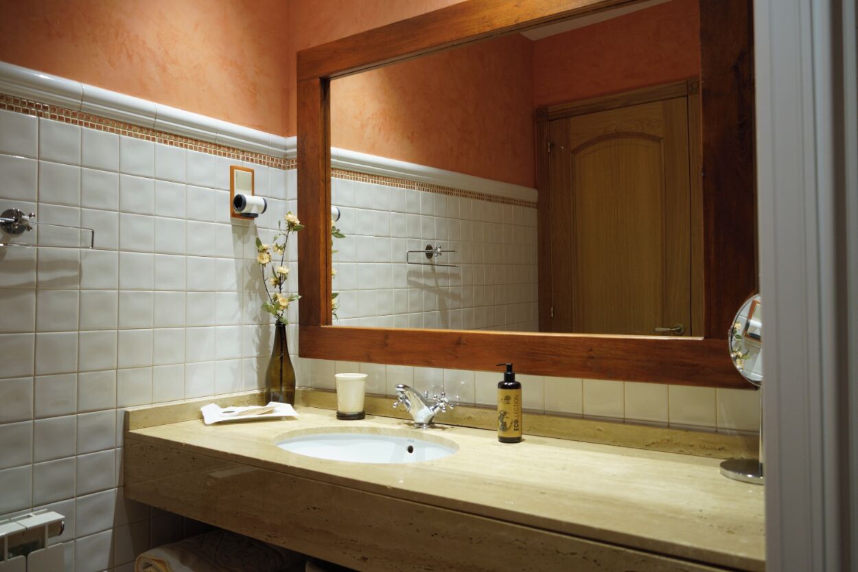 Un baño con un lavamanos color crema, un espejo y un armario de madera.