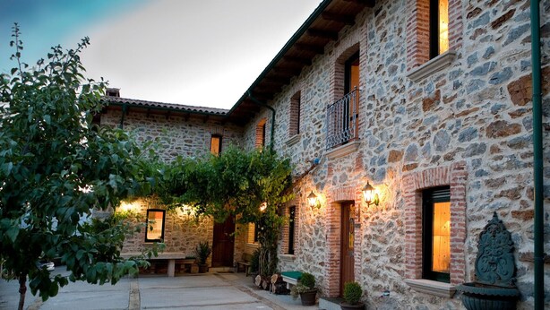 A stone building with a courtyard, featuring a bench, potted plants, and a large urn.