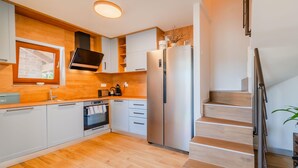 Una cuina moderna amb armaris de fusta, forn integrat, nevera d'acer inoxidable i una escala que condueix a un altre pis.