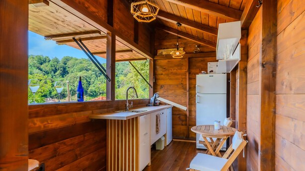 Una cabana de fusta senzilla amb una cuina americana, una zona de menjador amb taula i cadires, i una finestra que ofereix vistes a un paisatge forestal.