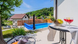 Un balcó amb piscina, taula amb fruita i begudes, i vista cap a cases i vegetació.