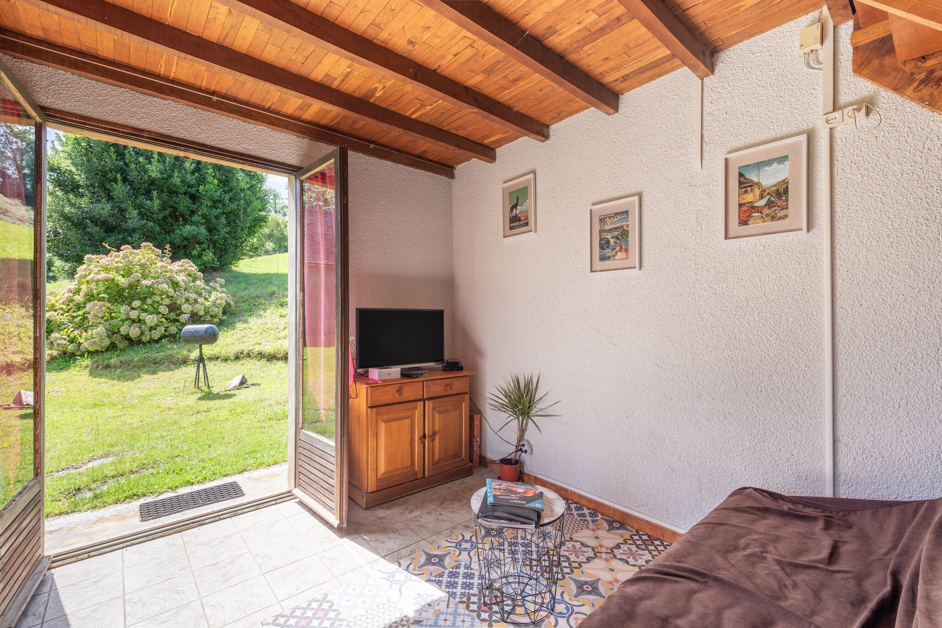 Una stanza con una porta vetrata scorrevole che si apre su un giardino, un armadio in legno, un televisore e un piccolo tavolo con libri.