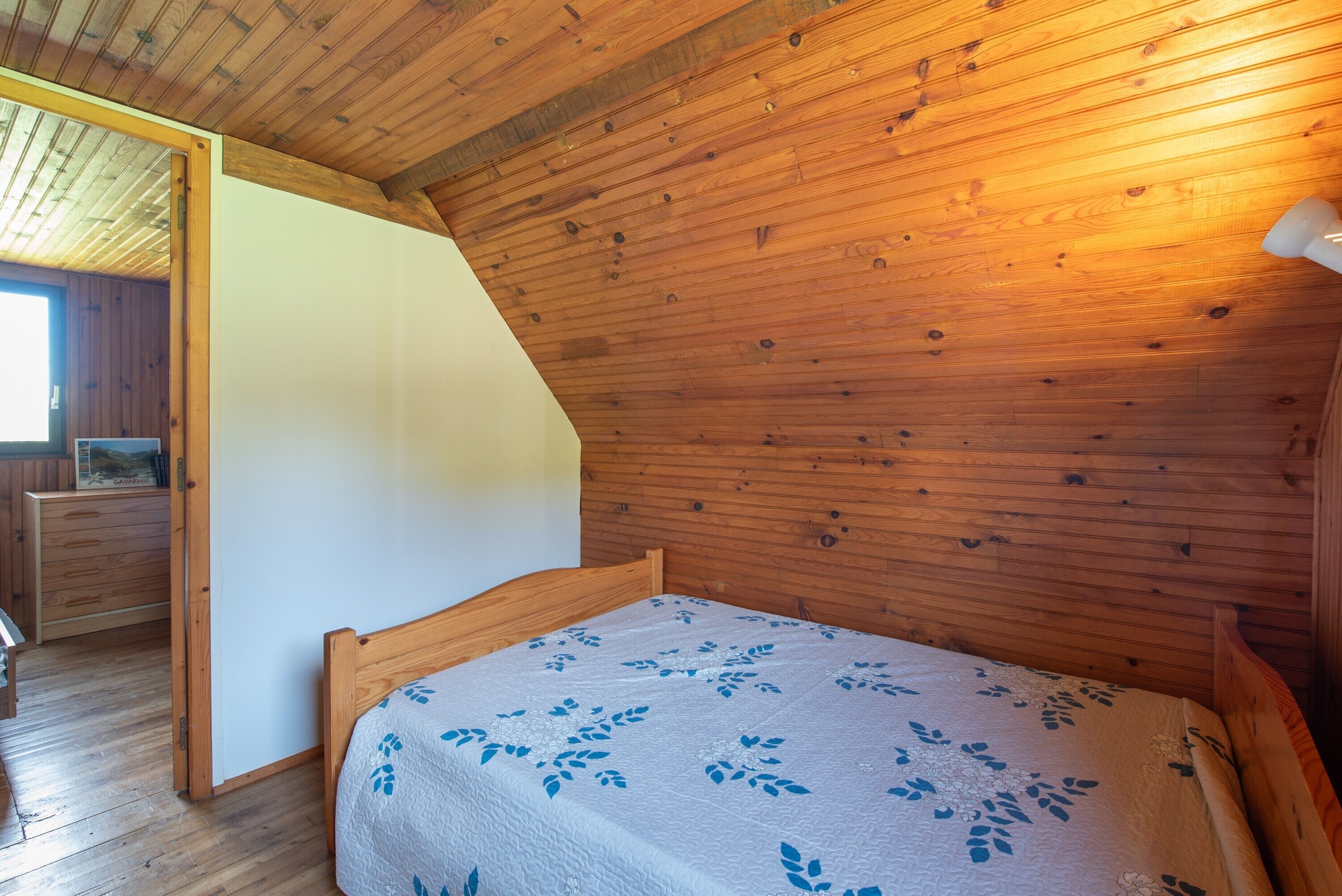 A bedroom with a wooden ceiling, a bed with a floral bedspread, and a wooden dresser.