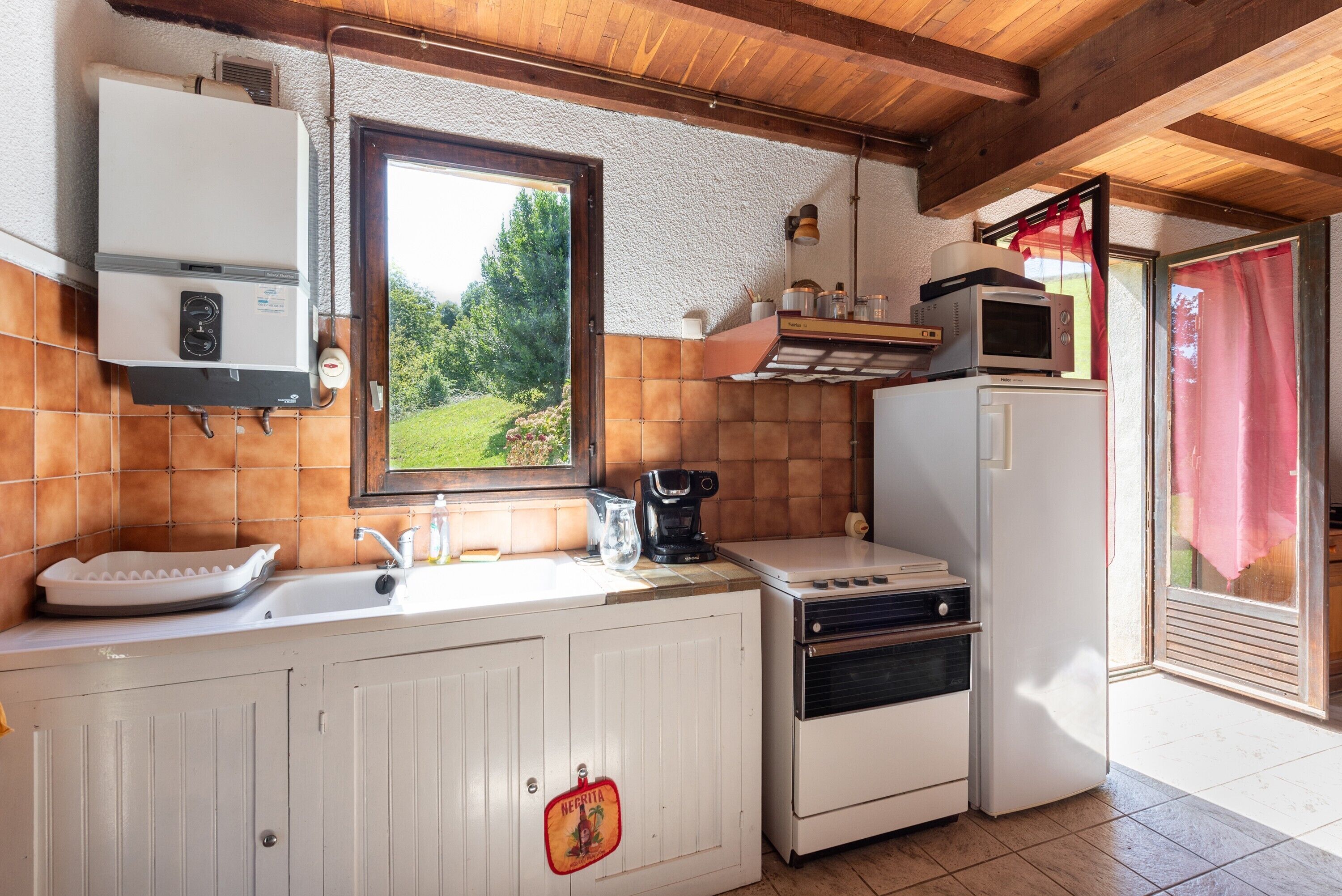 Une cuisine équipée d’un évier, d’une cuisinière, d’un four à micro-ondes et d’une fenêtre donnant sur un paysage verdoyant.
