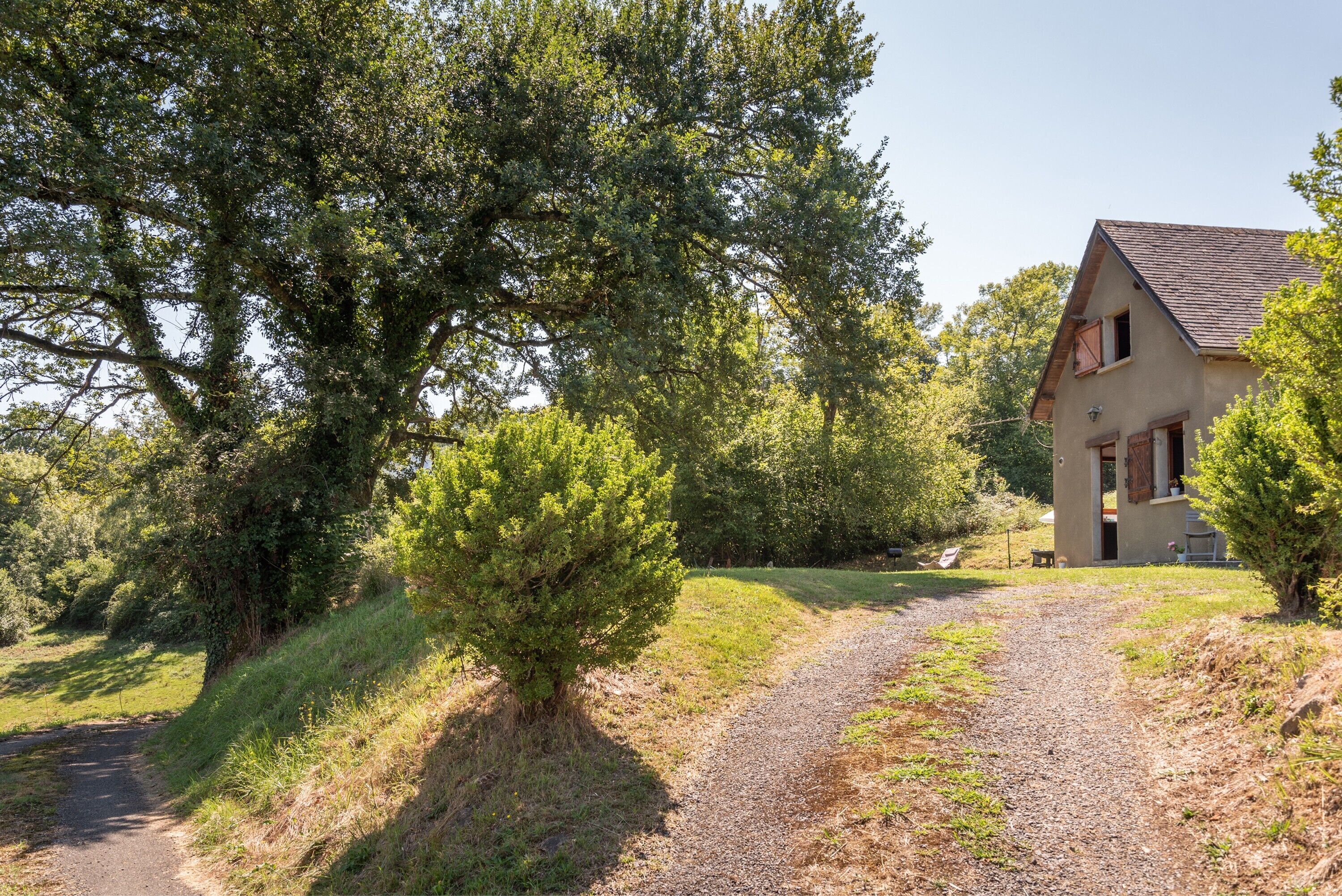 A house with a gravel driveway, surrounded by trees and greenery.