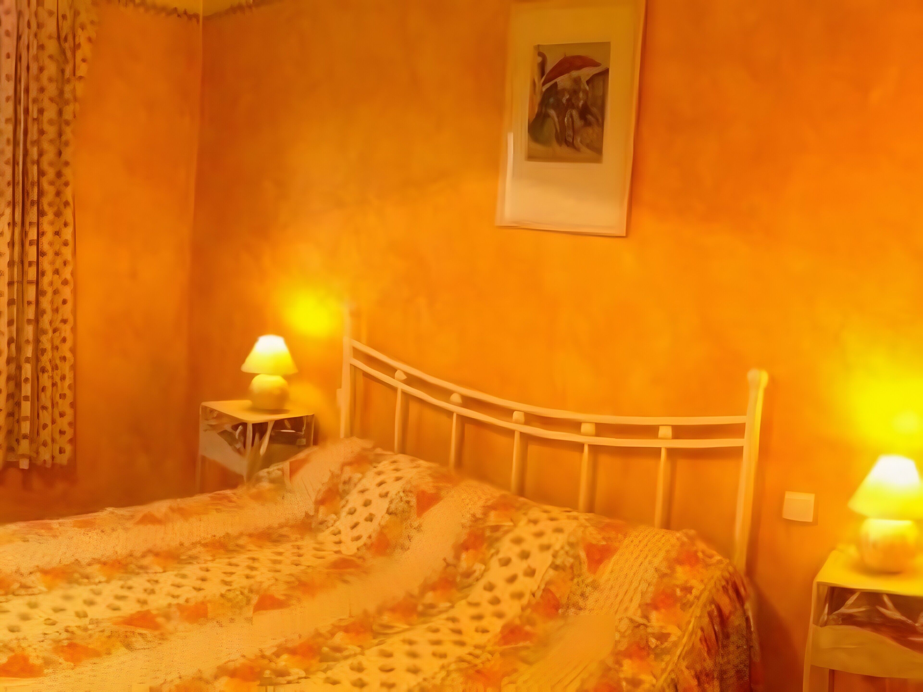 Une chambre à coucher avec un lit, deux tables de chevet avec des lampes, un rideau et un tableau au mur.