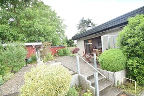 Et hus med en patio, et rødt skur og en have med forskellige planter.