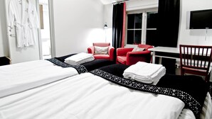 Une chambre d’hôtel avec deux lits, un fauteuil rouge, une petite table et un téléviseur.