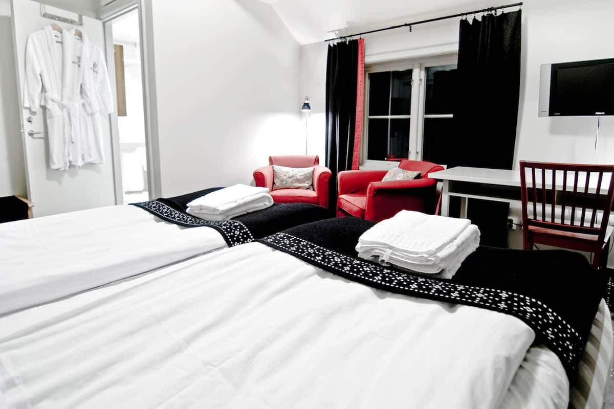 A hotel room with two beds, a red armchair, a small table, and a TV.
