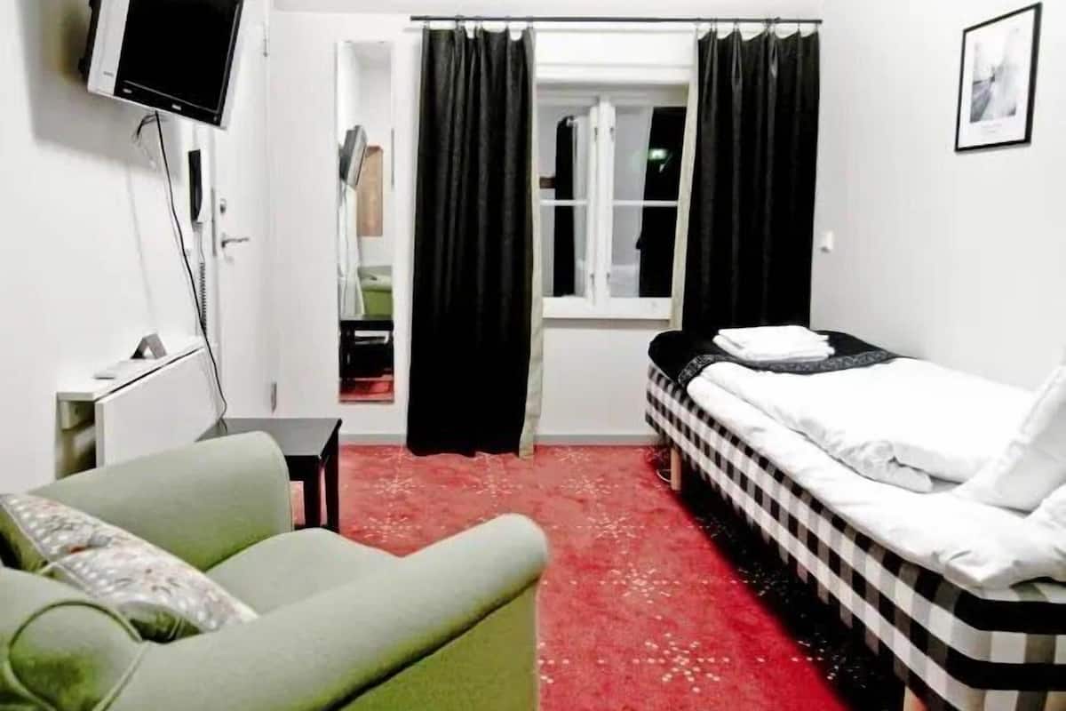 A hotel room with a bed, a green armchair, a TV, and a red carpet.