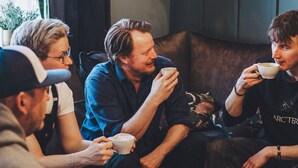 Un groupe de personnes est assis autour d’une table ronde, devant des assiettes, des tasses et une bougie.