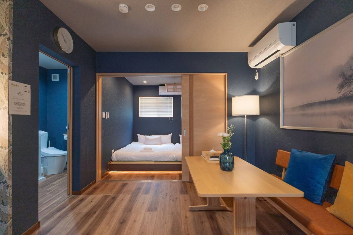 A hotel room with a bed, bedside table, lamp, and a view of the bathroom.