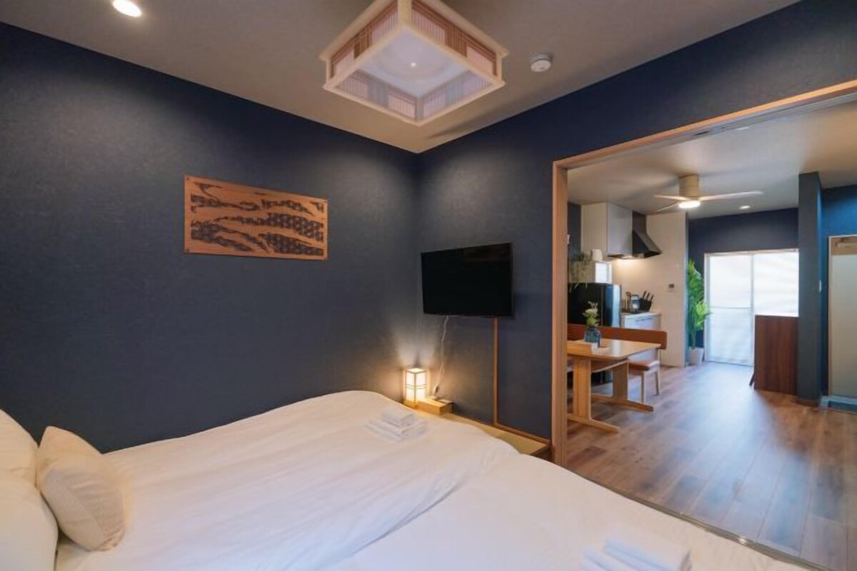 A bedroom with a bed, a flat-screen TV, a bedside lamp, and a wooden desk with a chair.