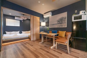 A modern room with a bed, a dining table with chairs, a refrigerator, and an air conditioning unit. - New open VERDE Tamade (Osaka)