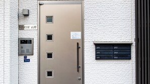 Rakennuksen sisäänkäynti, jossa on metalliovi, numeronäppäimistö ja pieni ikkuna, jossa on numeroituja tunnuslappuja.