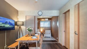 Moderni hotellihuone, jossa on puinen ruokapöytä, taulutelevisio, kello ja sohva.