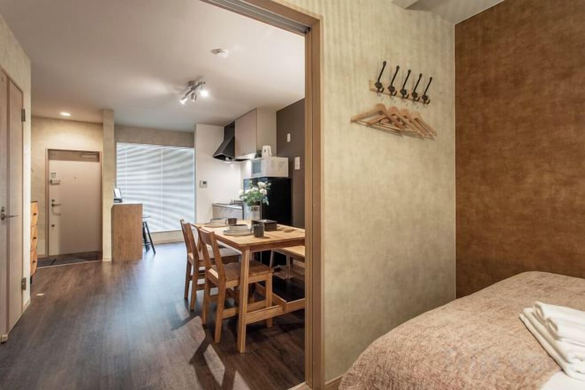 A hotel room with a bed, a dining table with chairs, a kitchen area, and a bathroom.
