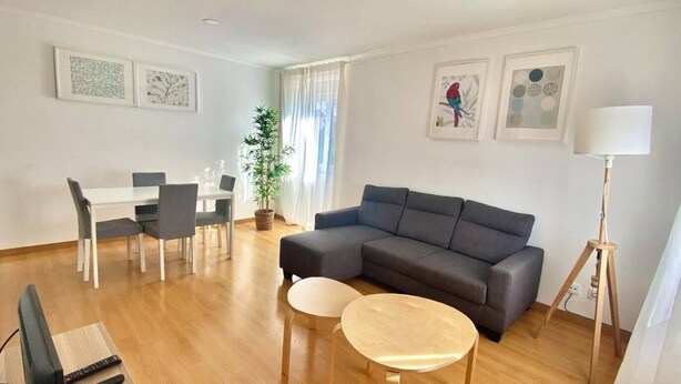 A modern living room with a grey sofa, two round coffee tables, a dining area with a white table and chairs, and a potted plant. - River view over Tage (Lisboa)