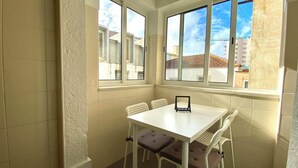 A corner room with a white table and four chairs, large windows with a view of buildings and a crane, and a textured wall. - River view over Tage (Lisboa)