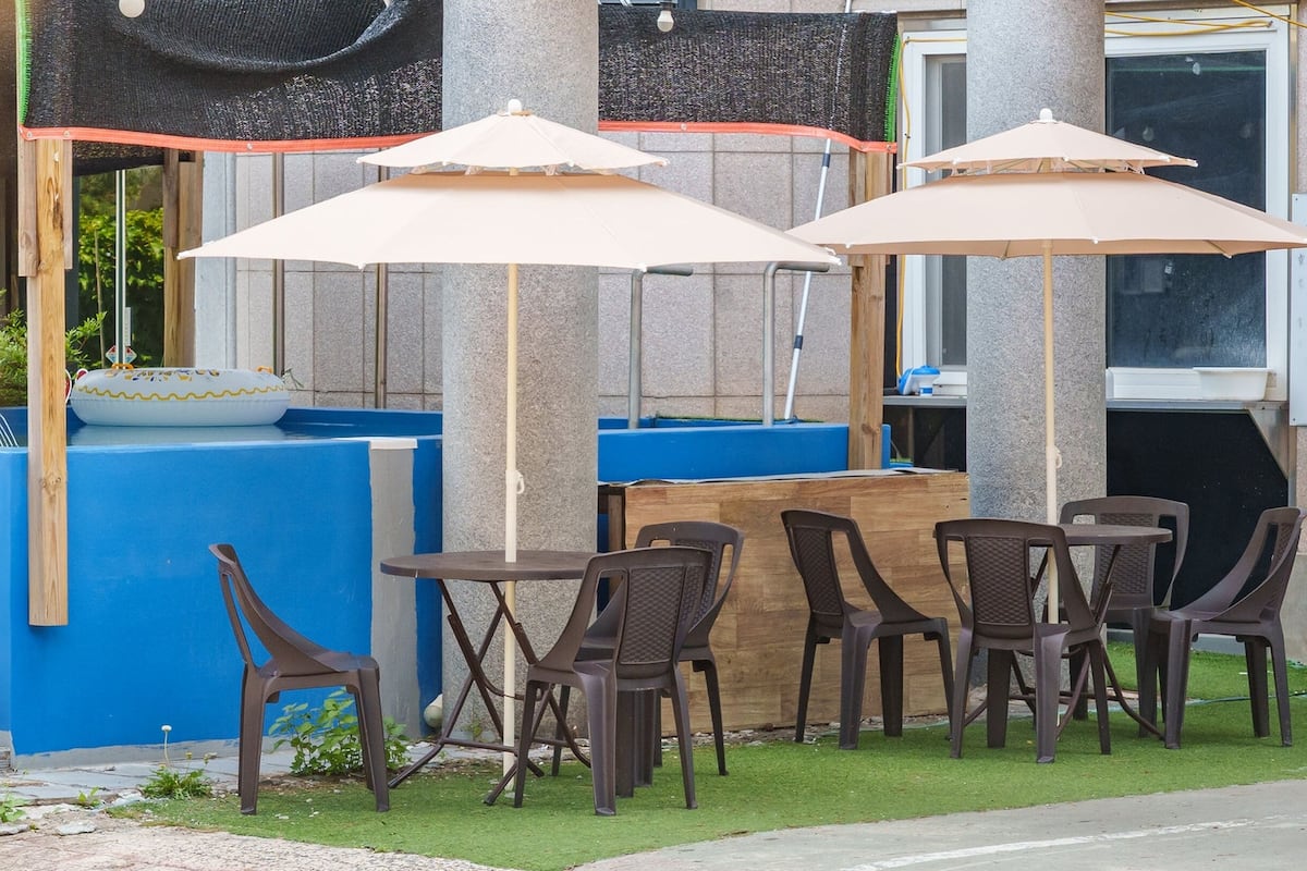 Outdoor seating with umbrellas, a blue pool, and a wooden table.