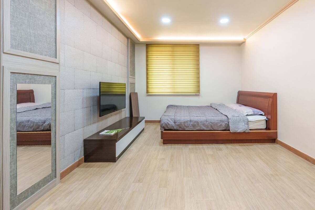 A bedroom with a bed, a TV mounted on the wall, and a window with blinds.
