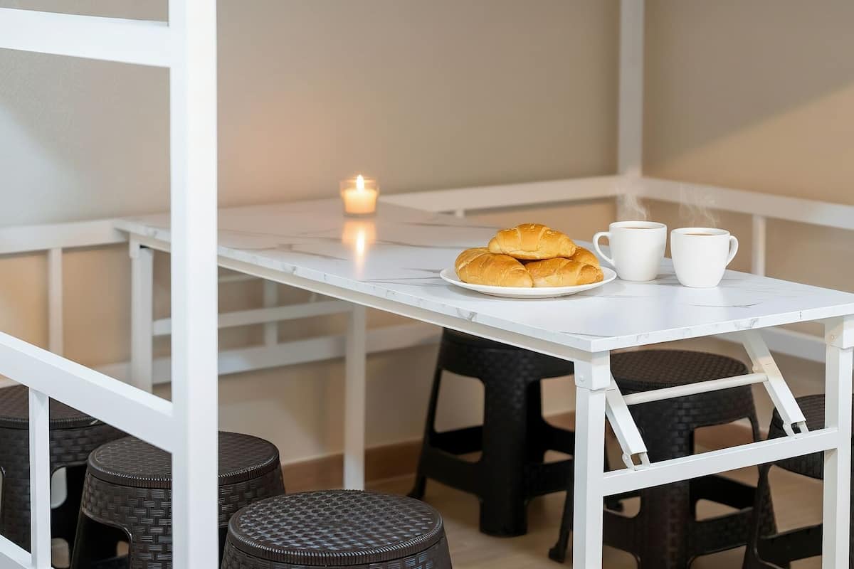 A white table with a plate of croissants and two cups of coffee, surrounded by wicker stools.