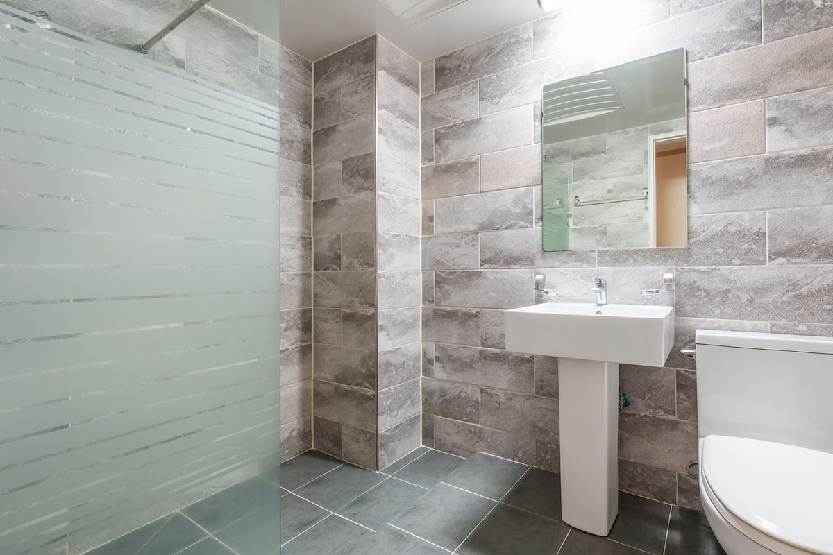 A bathroom with a glass shower enclosure, a white sink, and a toilet.