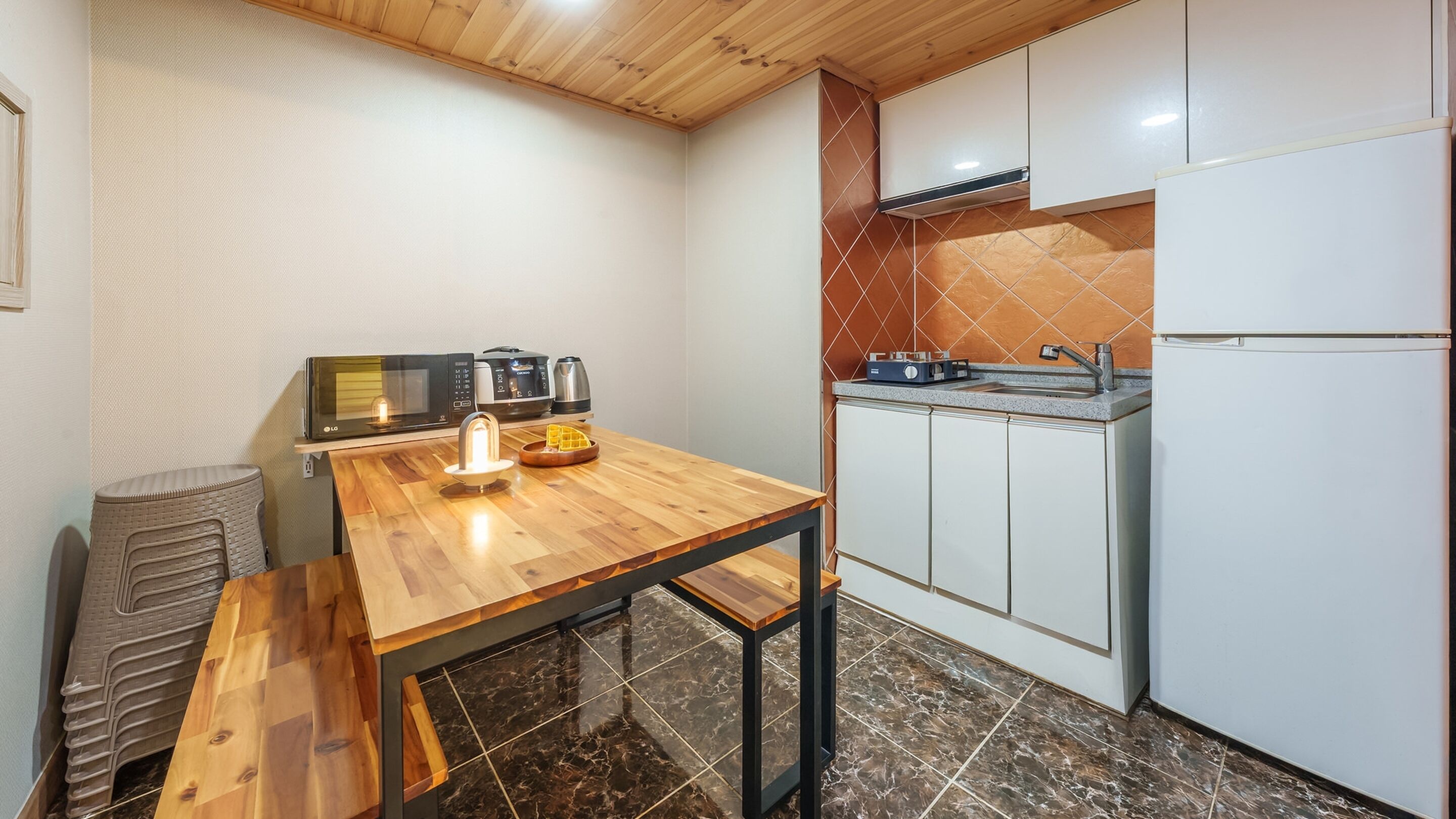 A compact kitchen with a wooden table, a microwave, a kettle, and a refrigerator.
