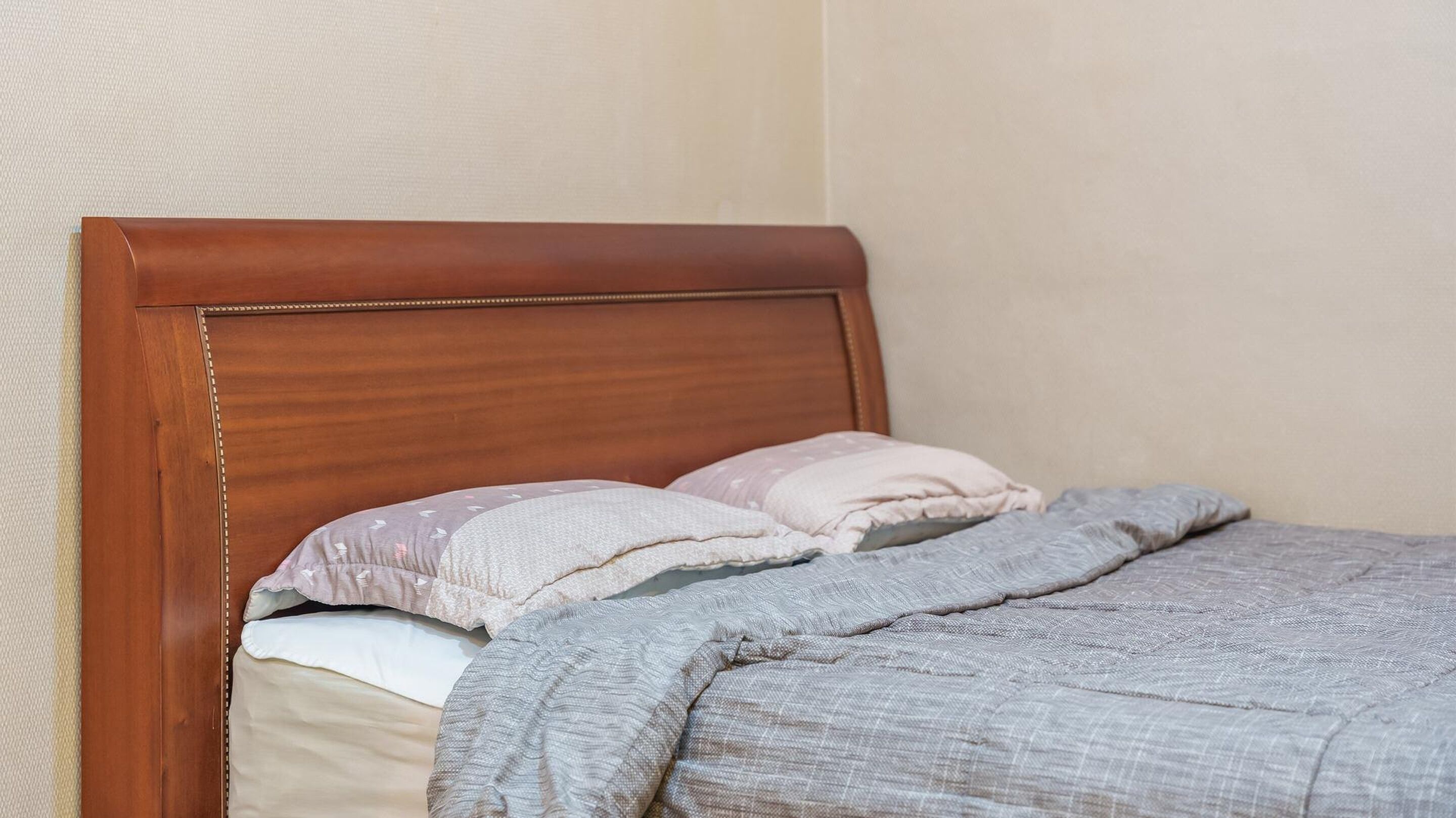 Una cama bien hecha con cabecera de madera, dos almohadas y una manta gris.