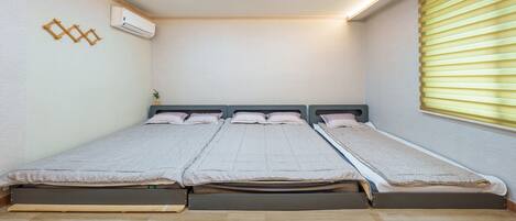 A room with a bed, an air conditioner, and a window with blinds.