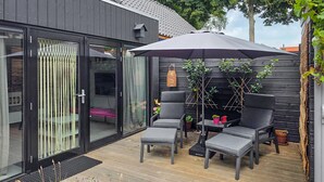 A modern outdoor patio with two grey chairs and a table, a large umbrella, and a small garden area with potted plants. - 1 bedroom lovely home in Heiloo (Heiloo)