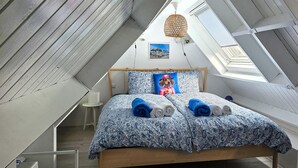 A bedroom with a sloped ceiling, a bed with patterned bedding, a hanging light fixture, and a framed picture on the wall. - 1 bedroom lovely home in Heiloo (Heiloo)