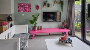 A modern living room with a pink bench, a flat-screen TV, and a variety of decorative items on shelves. - 1 bedroom lovely home in Heiloo (Heiloo)