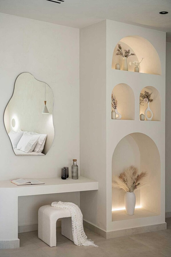 Quarto moderno e minimalista com um espelho grande, um banco branco e uma prateleira suspensa com vasos.